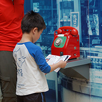 赤い公衆電話の前でワークブックを広げる親子の写真